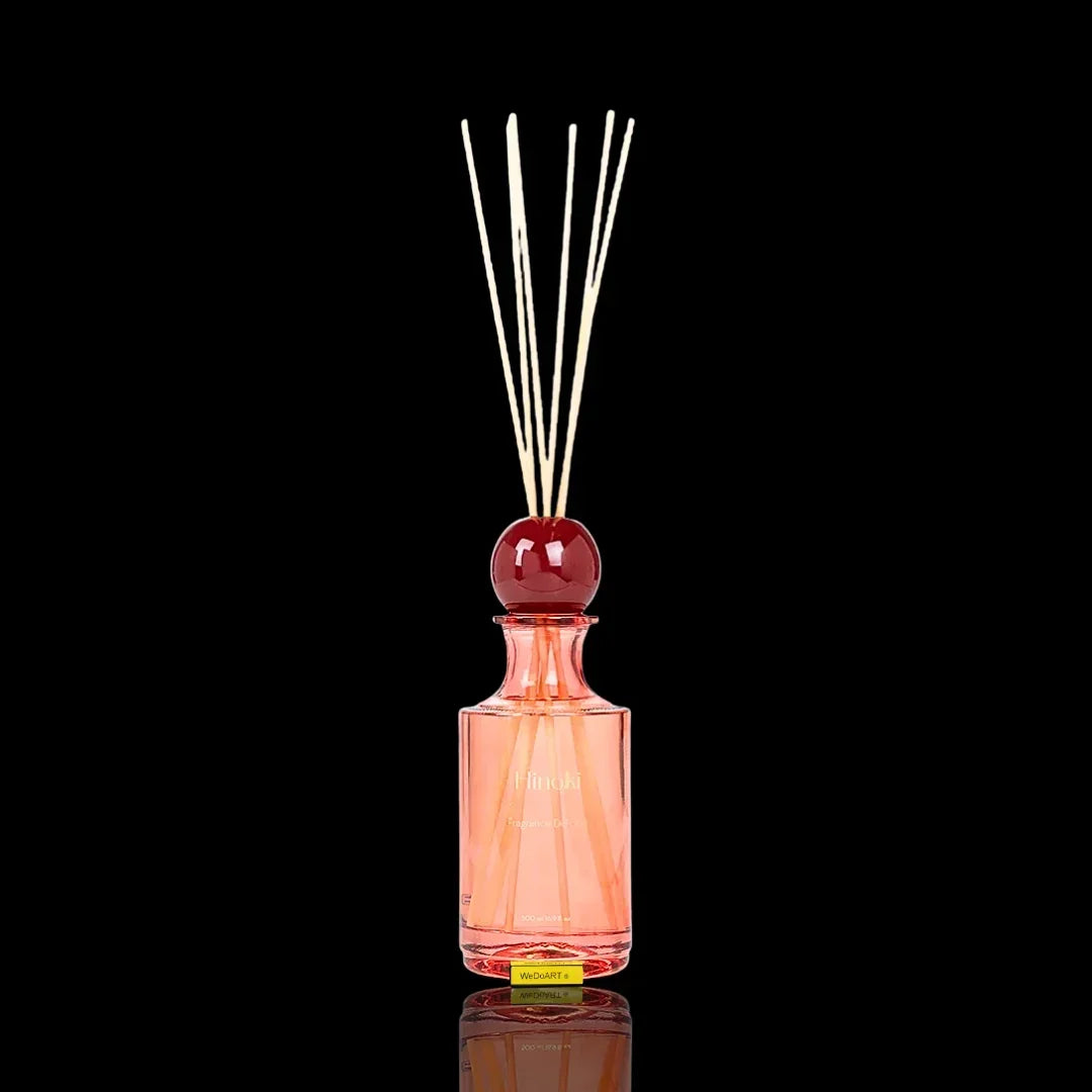 Pink glass fragrance diffuser bottle with wooden reeds and a red decorative topper.
