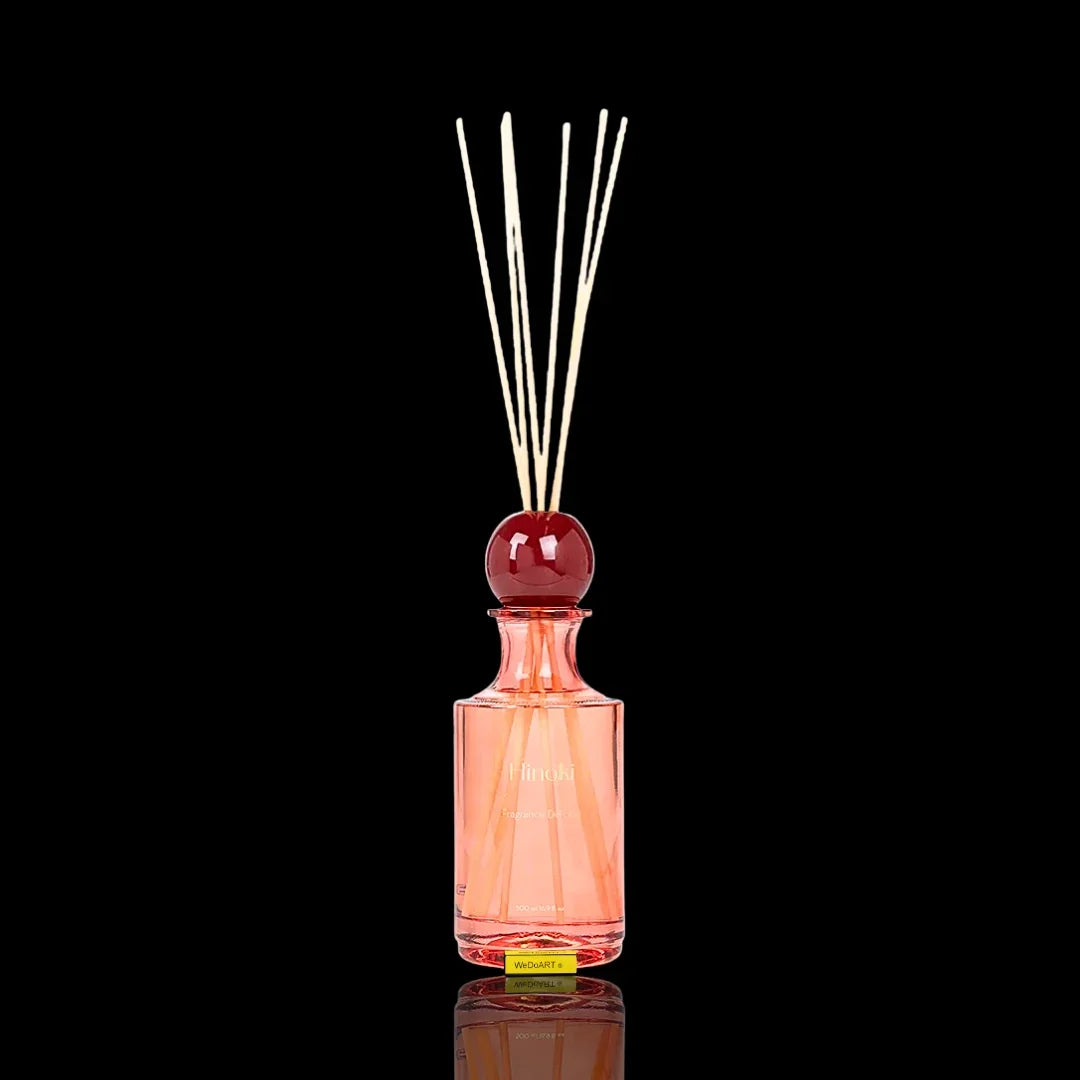 Pink glass fragrance diffuser bottle with wooden reeds and a red decorative topper.