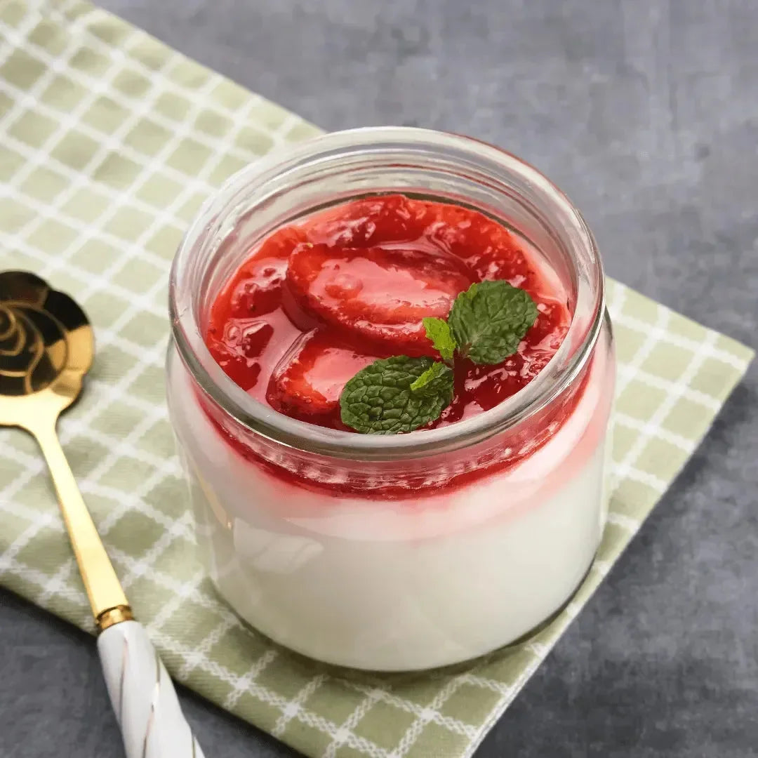 Creamy vanilla pudding in a glass jar topped with strawberry sauce and a mint leaf