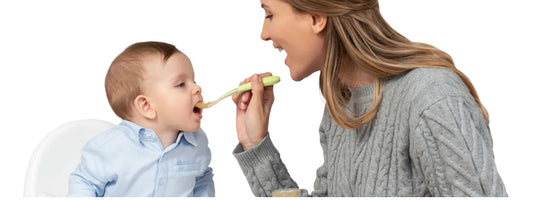 Mother feeding baby with spoon, both smiling, on white background