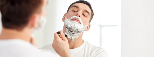 Man shaving his face with foam in front of bathroom mirror, skincare routine concept