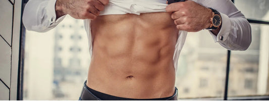 Man lifting shirt to reveal toned abs, wearing dress shirt and watch, in modern room