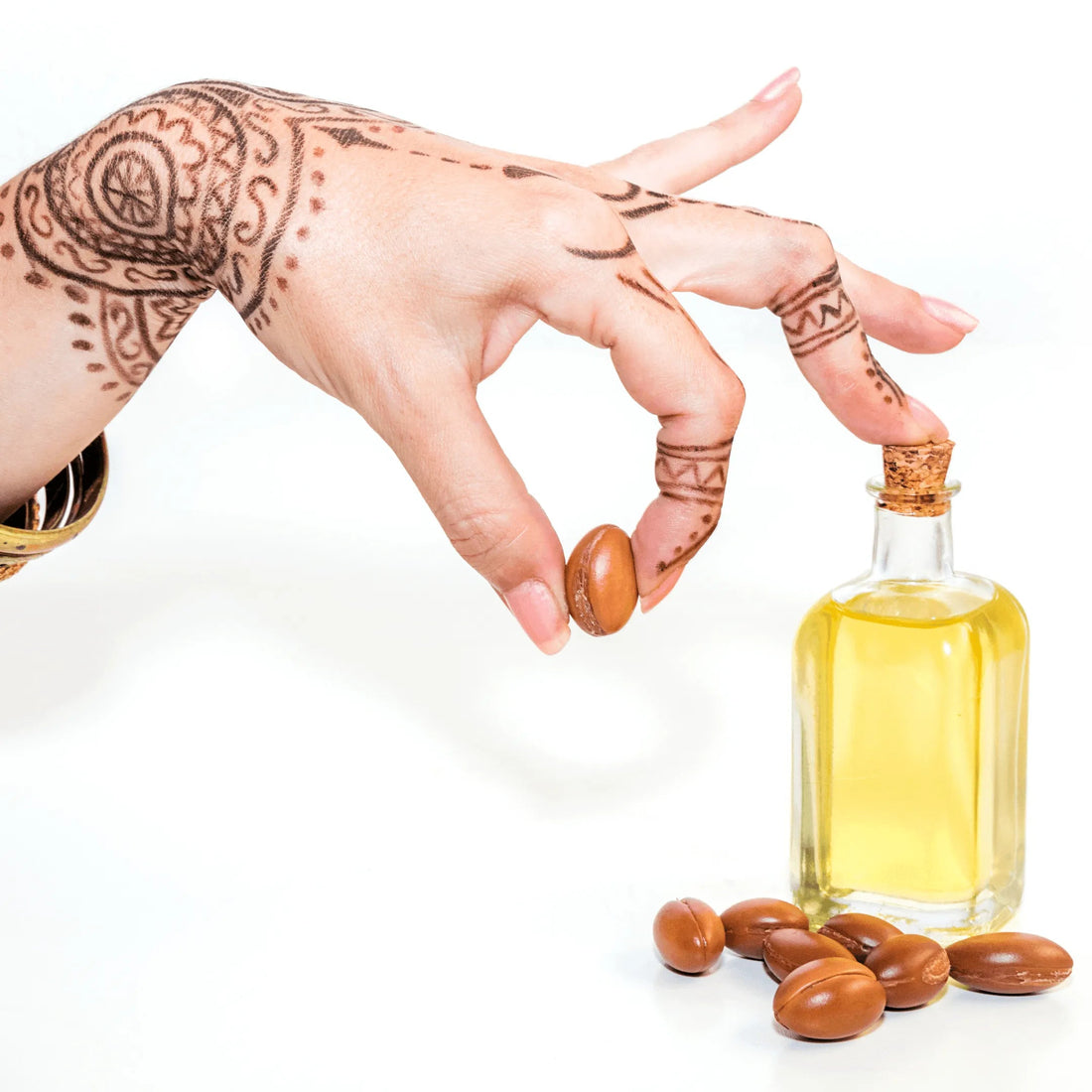 Hand with henna holding argan nut near bottle of argan oil for skincare on white background
