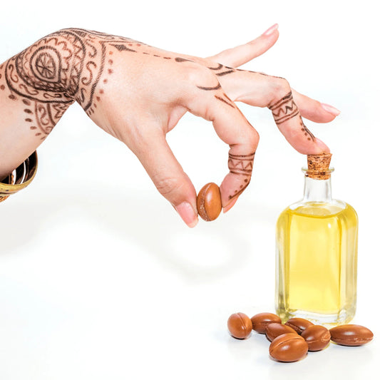 Hand with henna holding argan nut near bottle of argan oil for skincare on white background