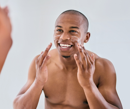 Smiling man applying facial cream during his skincare routine, promoting healthy skin care.