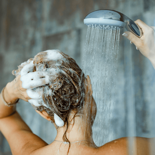 Woman washing hair with shampoo in shower, highlighting healthy skincare and haircare