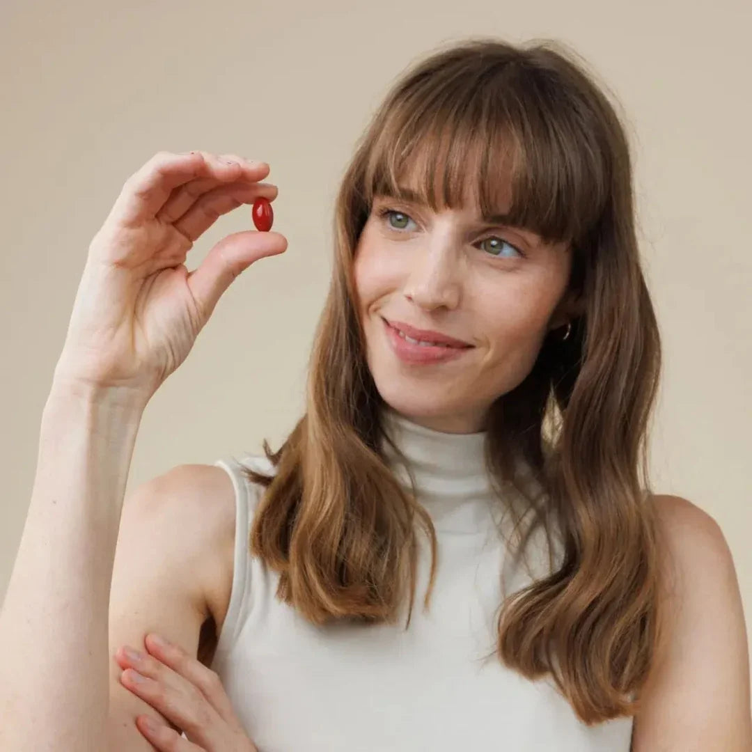A woman holding a small red skincare capsule between her fingers.