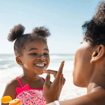 A parent applies Dr. Fischer ULTRASOL kids sunscreen lotion to a child's face at the beach