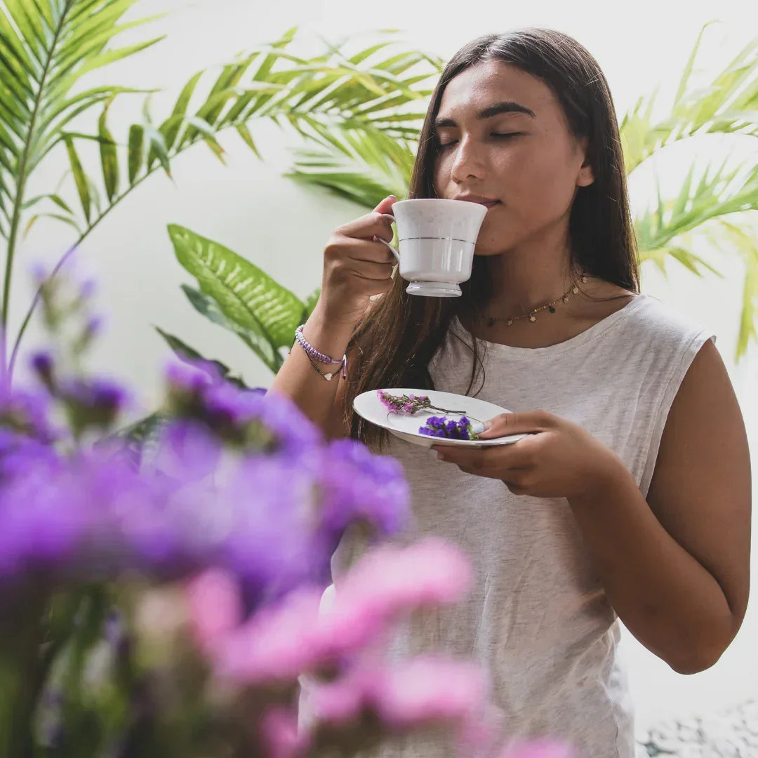 Woman enjoying a cup of herbal Tibetan tea among palm leaves and purple flowers