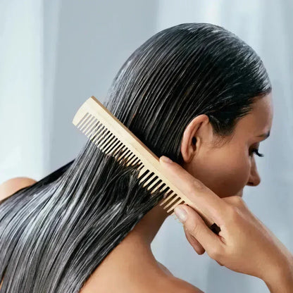 Woman combing wet, shiny hair with a wooden comb after applying a hair mask