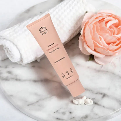 LALINE Cherry Blossom Body Cream tube lying on marble with a cream swatch beside a white towel and a pink rose