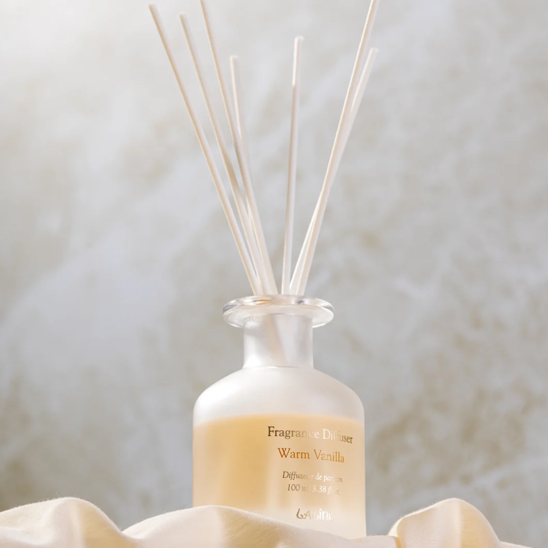 Frosted bottle of the Laline Warm Vanilla reed diffuser with white reeds, styled on soft cream fabric