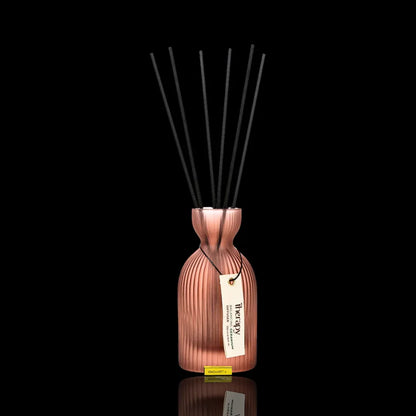 Aufgestellter LALINE Geranium Fragrance Diffuser im gerippten Glasgefäß in Roségold mit schwarzen Stäbchen und cremefarbenem Anhänger