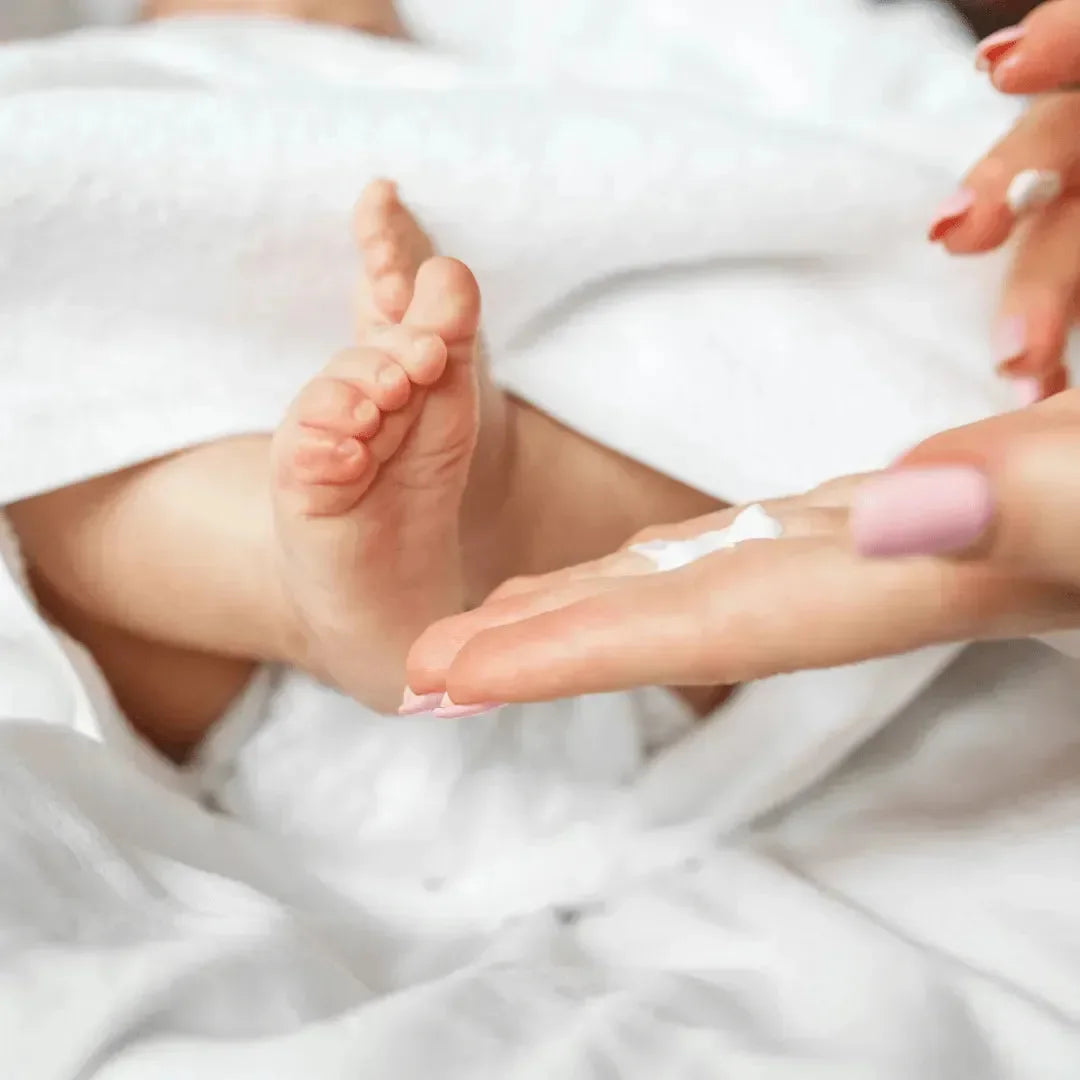 Baby feet on a white towel with a mother's hand holding a dab of white lotion