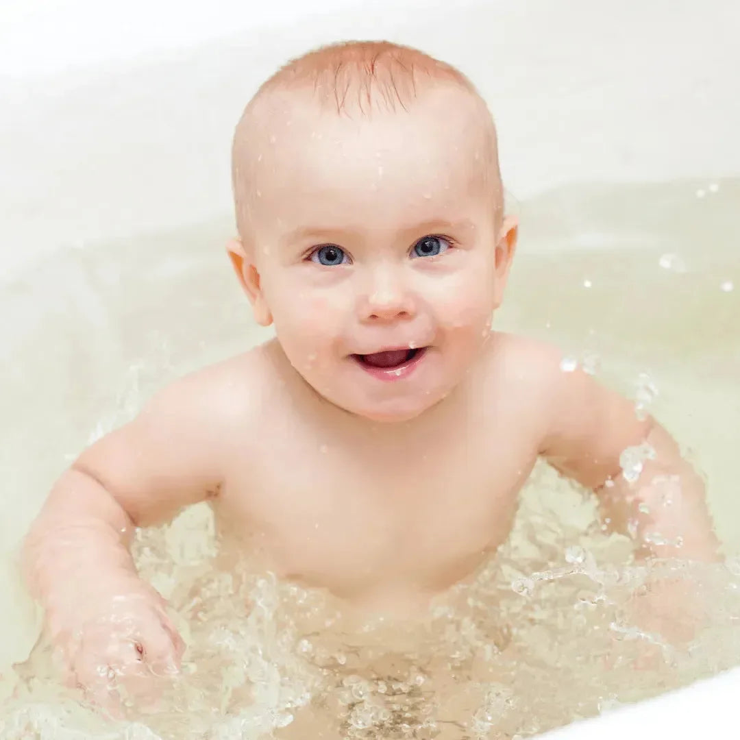 Smiling baby splashing in a bath filled with soft, pale water