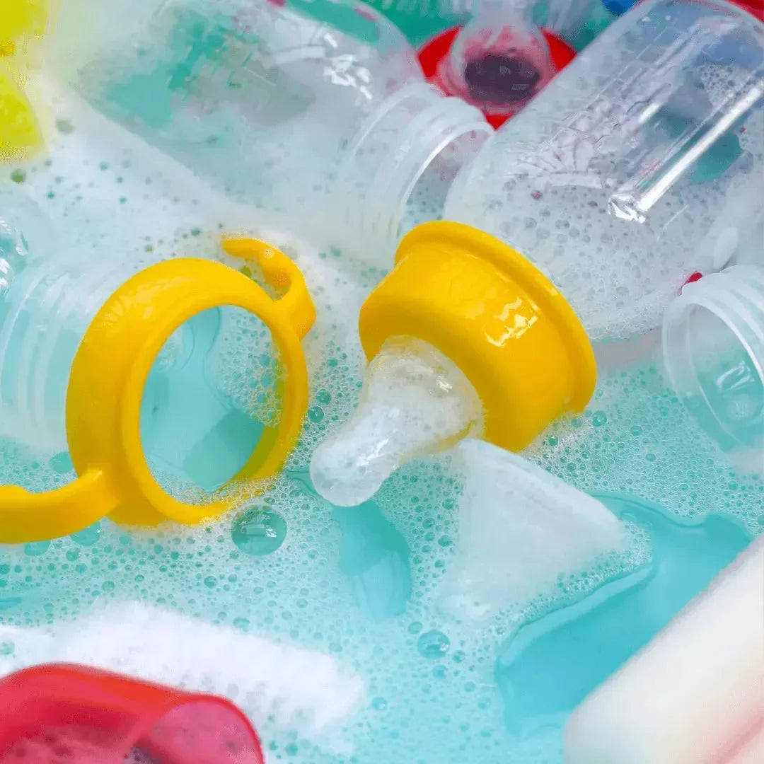 Baby bottles, nipples, and pacifier rings soaking in soapy water with foam bubbles