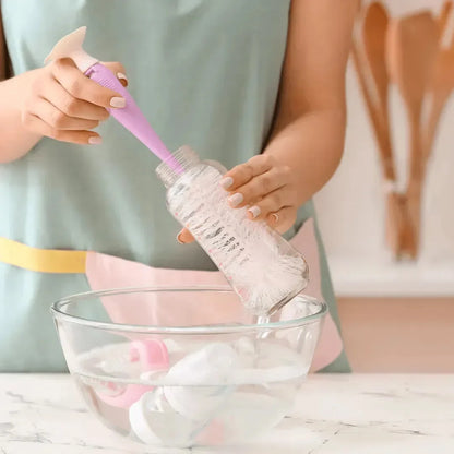 Woman scrubbing a baby bottle with a brush above a bowl of soapy water holding a pacifier