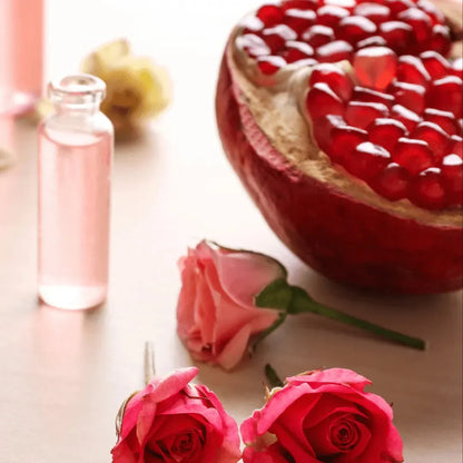 Halved pomegranate with red seeds, pink roses and a small oil bottle