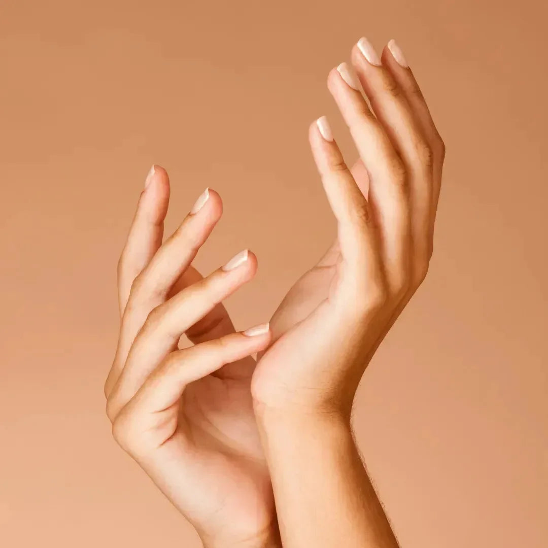 Two hands with neatly shaped natural nails against a warm peach background