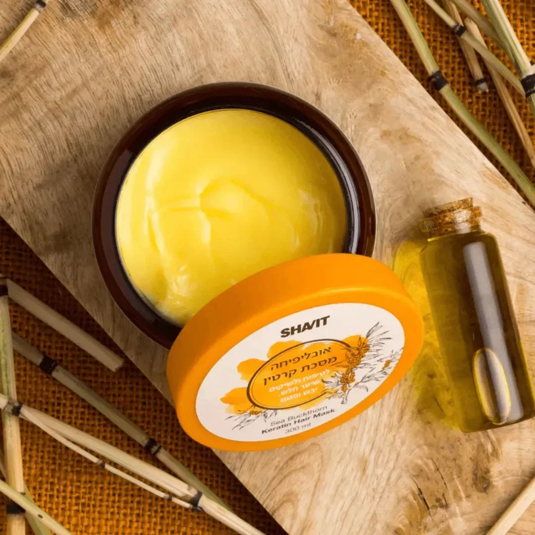 Open jar of golden sea buckthorn keratin hair mask beside a small bottle of oil on a wooden board