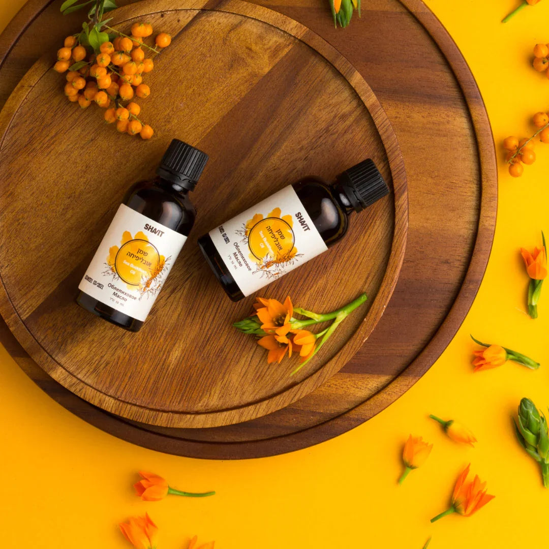 Two SHAVIT sea buckthorn oil bottles on round wooden boards with orange berries and flowers on a yellow background