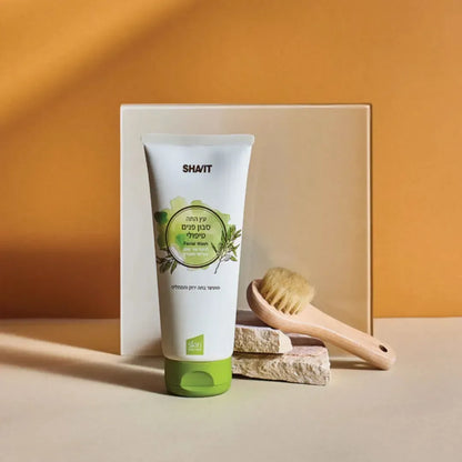 SHAVIT tea tree facial wash tube with a wooden facial brush on stone against an orange backdrop