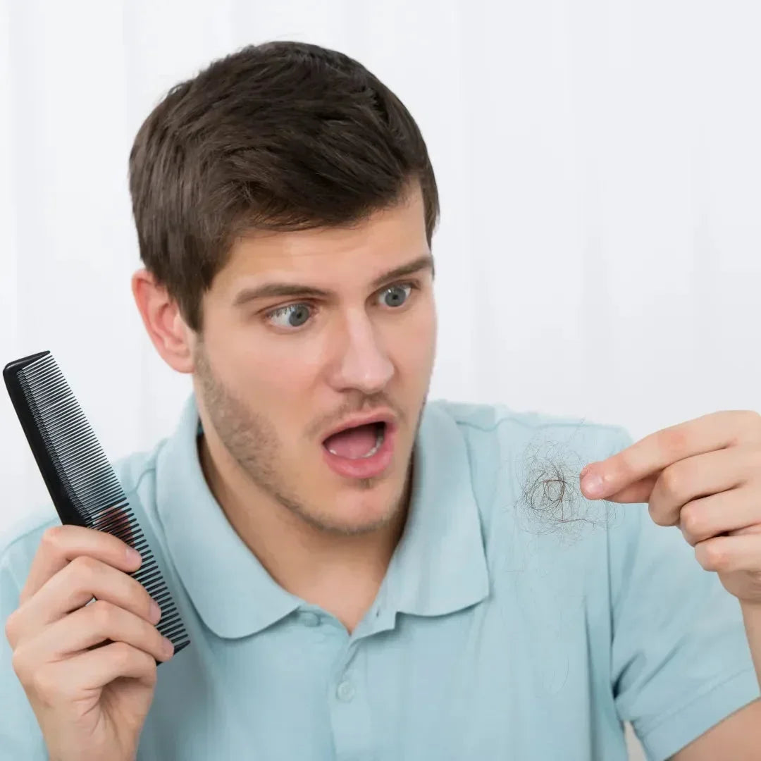 Young man in a light blue polo shirt holding a comb and looking at hair strands between his fingers