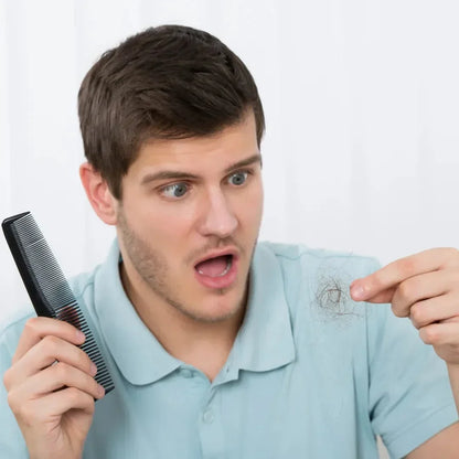 Young man in a light blue polo shirt holding a comb and looking at hair strands between his fingers